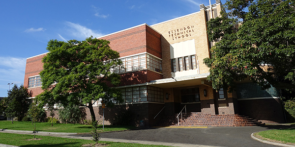 front of red and yellow brick building with 'essendon technical school' sign.